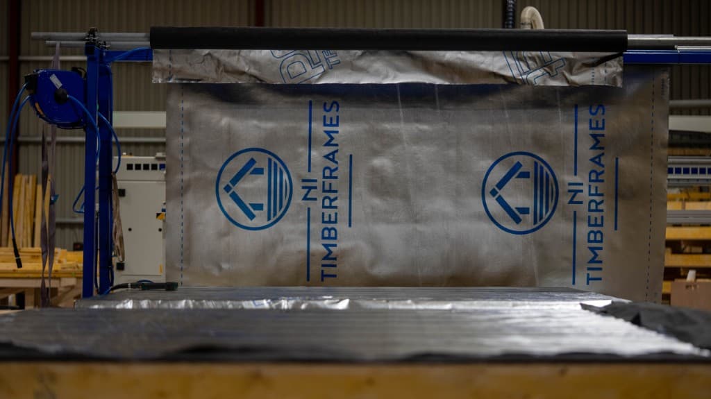 Worker applying insulation to timber frame panel